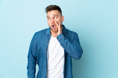 Mavi arka planda izole edilmiş Rus yakışıklı adam yan tarafa bakarken sürpriz bir jest yapıyor.
