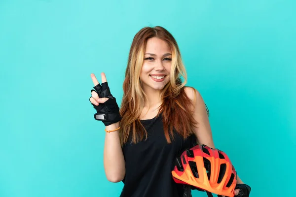 Junges Radfahrermädchen Vor Blauem Hintergrund Lächelt Und Zeigt Siegeszeichen — Stockfoto