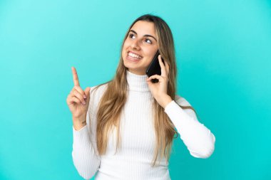 Mavi arka planda izole edilmiş cep telefonu kullanan beyaz bir kadın harika bir fikre işaret ediyor.