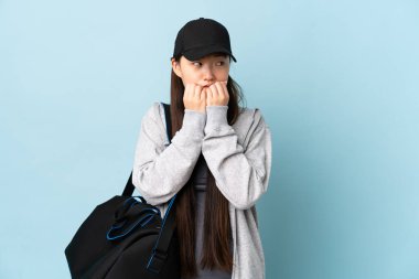 Spor çantasıyla genç bir Çinli kadın mavi arka planda gergin ve korkmuş bir şekilde elleriyle suni teneffüs yapıyor.
