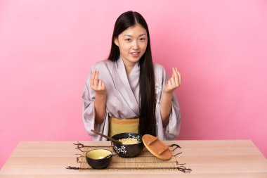 Kimono giyen ve erişte yiyen genç Çinli kız para hareketi yapıyor.