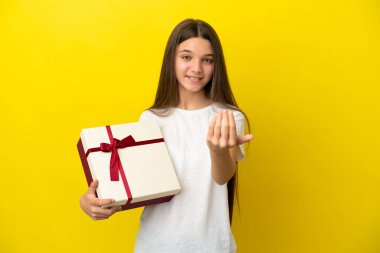 İzole edilmiş sarı arka planda bir hediye taşıyan küçük bir kız, bizi davet ediyor. Gelmene sevindim.