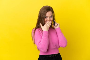 İzole edilmiş sarı arka planda cep telefonu kullanan genç kız mutlu ve gülümsüyor.