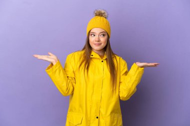 Yağmura dayanıklı bir ceket giyen genç kız mor arka planda kuşkuları var ve ellerini kaldırıyor.