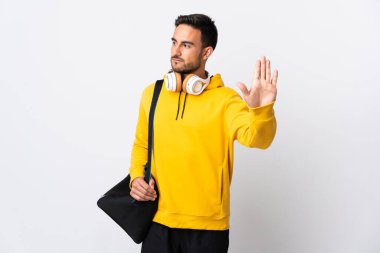 Spor çantalı genç adam beyaz arka planda izole edilmiş. Durma hareketi yapıyor ve hayal kırıklığına uğruyor.
