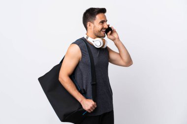Spor çantalı genç adam beyaz arka planda izole edilmiş cep telefonuyla sohbet ediyor.