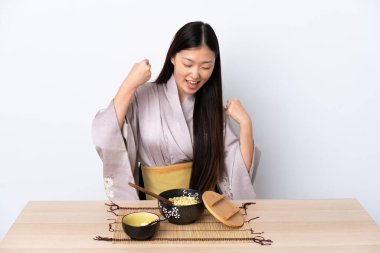 Kimono giyip erişte yiyen genç Çinli kız zaferi kutluyor.