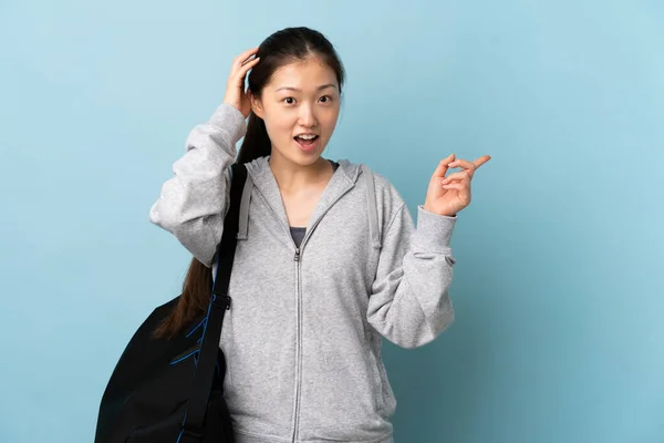 Ung Kinesisk Kvinne Med Sportsbag Isolert Blå Bakgrunn Overrasket Pekende – stockfoto
