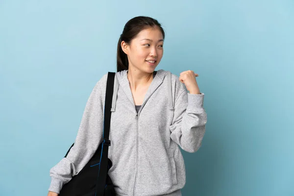 年轻的中国女运动员 背着运动包 蓝色背景 指着侧面展示自己的产品 — 图库照片