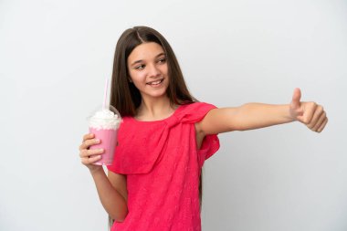 İzole edilmiş beyaz arka planda çilekli milkshake 'i olan küçük kız baş parmak işareti yapıyor.
