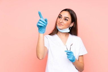 Pembe arkaplanda izole edilmiş kadın dişçi araçları şeffaf ekrana dokunuyor