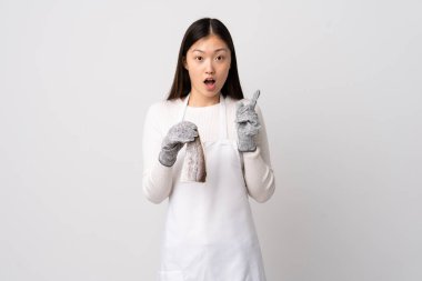 Çinli balıkçı önlük takıyor ve çiğ balığı izole edilmiş beyaz arka planda tutuyor. Çözümün farkına varmak için parmağını kaldırıyor.