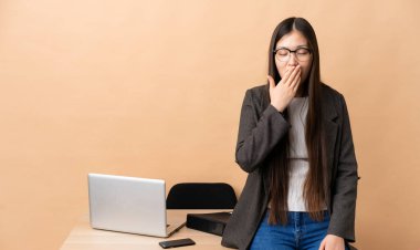 İş yerinde Çinli bir iş kadını esniyor ve ağzı açık bir şekilde elleriyle ağzını kapatıyor.