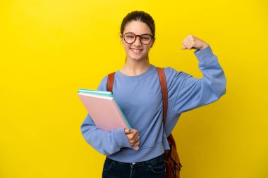 İzole edilmiş sarı arka planda öğrenci bir kadın güçlü bir jest yapıyor.