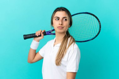 Mavi arka planda izole edilmiş genç beyaz kadın tenis oynuyor.