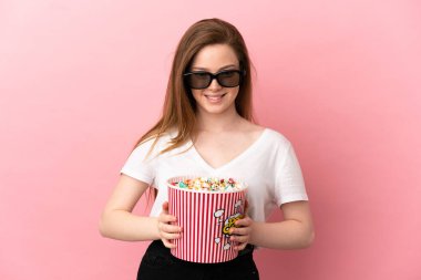 Üç boyutlu gözlüklü ve elinde koca bir kova patlamış mısırla izole pembe arka planı olan genç bir kız.