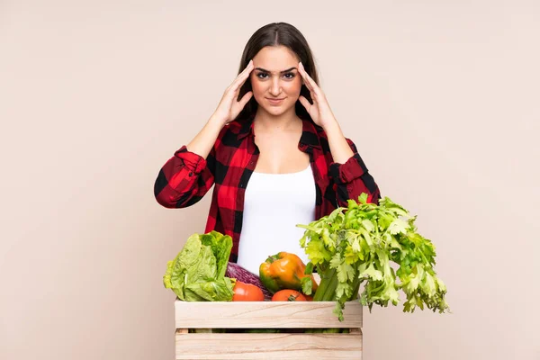 Farmer with freshly picked vegetables in a box isolated on beige background unhappy and frustrated with something. Negative facial expression