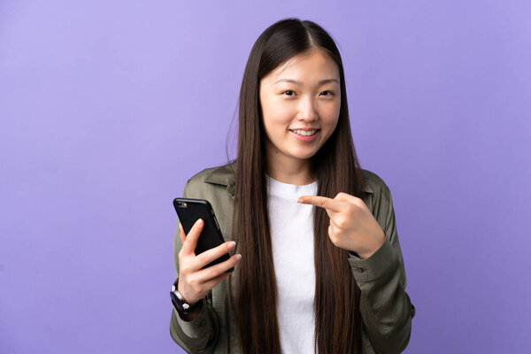 Молодая китаянка использует мобильный телефон на изолированном фиолетовом фоне и направляет его
