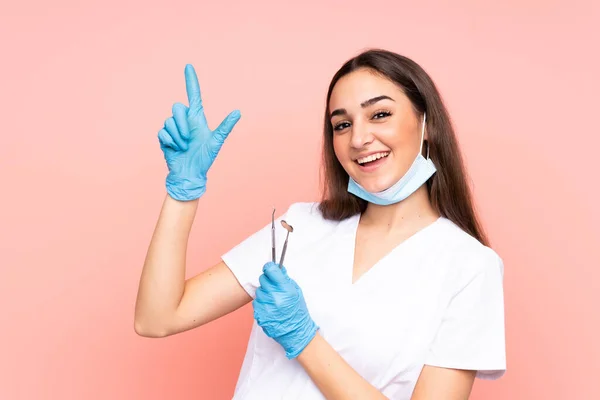 Γυναίκα Οδοντίατρος Κρατώντας Εργαλεία Που Απομονώνονται Ροζ Φόντο Δείχνοντας Δείκτη — Φωτογραφία Αρχείου