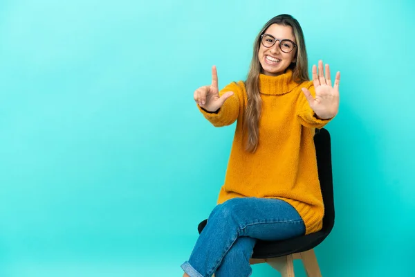 年轻的高加索女人坐在蓝色背景的椅子上 手指头数到七 — 图库照片