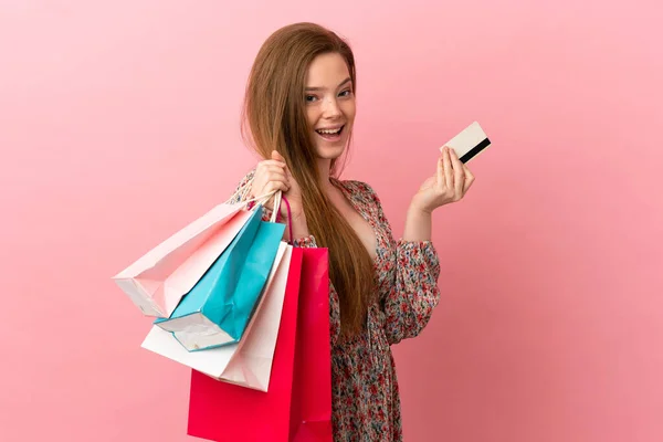 一个带着购物袋和信用卡的年轻姑娘 她的背景是孤立的粉色 — 图库照片