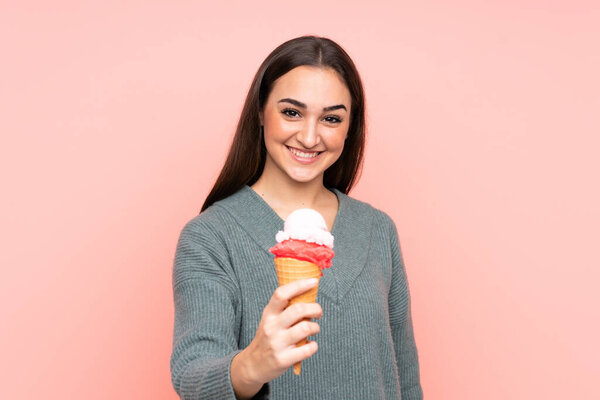 Young woman holding a cornet ice cream isolated on pink background with happy expression