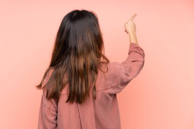 Pembe arka planda izole edilmiş genç beyaz kadın işaret parmağıyla işaret ediyor.