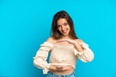 Mavi arka planda izole edilmiş genç beyaz kadın bir ilan vermek için avucunun içinde hayali bir fotokopi makinesi tutuyor.