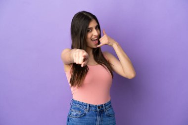 Mor arka planda izole edilmiş genç, beyaz bir kadın telefon hareketi yapıyor ve ön tarafı işaret ediyor.