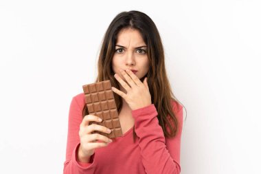 Pembe arka planda izole edilmiş beyaz bir kadın çikolata tableti alıyor ve şaşırıyor.