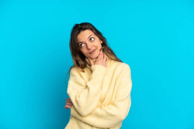 Mavi arka planda izole edilmiş genç beyaz kadın gülümserken yukarı bakıyor.