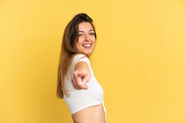 Sarı arka planda izole edilmiş genç beyaz kadın mutlu bir ifadeyle öne işaret ediyor.