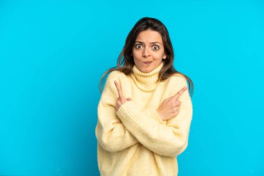 Mavi arka planda izole edilmiş genç beyaz kadın, yan taraftakilerin şüphelerine işaret ediyor.