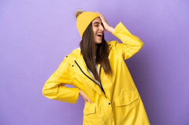 Mor arka planda izole edilmiş, yağmura dayanıklı bir palto giyen beyaz bir kadın.