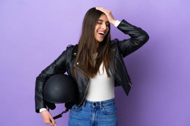 Motosiklet kasklı beyaz bir kadın, mor arka planda izole edilmiş, gülümsüyor.