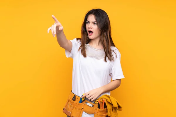 Young electrician woman over isolated on yellow background pointing away
