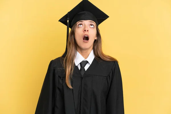 Fiatal Egyetemi Diplomás Elszigetelt Sárga Háttér Néz Fel Meglepett Kifejezés — Stock Fotó