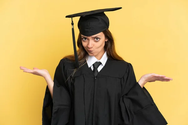 Junge Universitätsabsolventin Auf Gelbem Hintergrund Mit Zweifeln Beim Händeheben Isoliert — Stockfoto