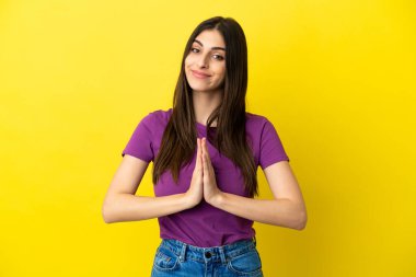 Sarı arka planda izole edilmiş genç beyaz kadın avuç içlerini bir arada tutuyor. İnsan bir şey ister.