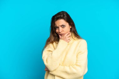 Kafkasyalı genç bir kadın mavi arka planda izole edilmiş. Şüpheleri var.