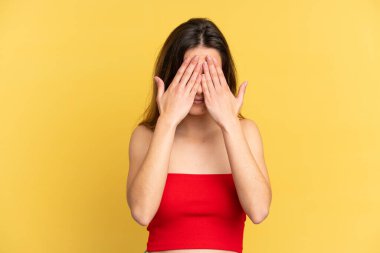 Sarı arka planda izole edilmiş genç, beyaz bir kadın elleriyle gözlerini kapatıyor.