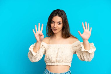 Mavi arka planda izole edilmiş genç beyaz kadın parmaklarıyla dokuzu sayıyor.