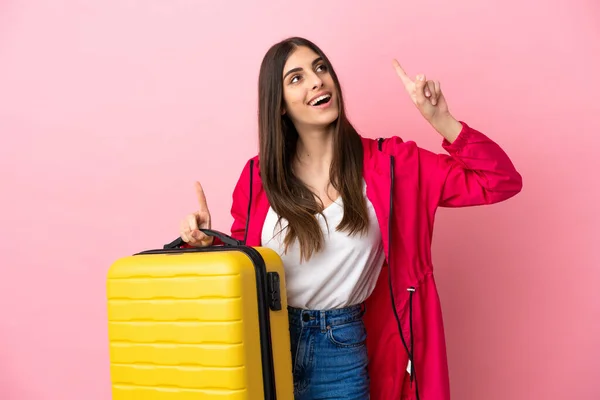 年轻的高加索女人 带着旅行箱和指点 带着粉红的背景在度假时被隔离 — 图库照片