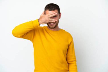 Genç Brezilyalı bir adam beyaz arka planda izole edilmiş gözleri elleriyle kaplıyor ve gülümsüyor.