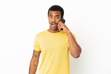 Afro-Amerikalı yakışıklı adam, izole edilmiş beyaz arkaplan üzerinde cep telefonu kullanıyor ve şaşırmış yüz ifadesi var.