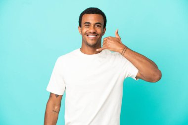 İzole edilmiş mavi arka planda Afro-Amerikalı yakışıklı bir adam telefon jesti yapıyor. Bana geri dönüş işareti ver.