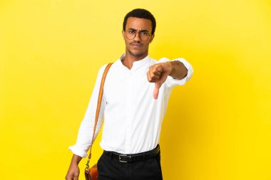 Afrika kökenli Amerikalı iş adamı sarı arka planda, olumsuz ifadeyle baş parmağını gösteriyor.