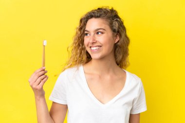 Sarı arka planda dişlerini fırçalayan beyaz bir kadın.