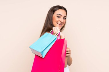 Beyazlı genç bir kadın bej arka planda izole edilmiş. Elinde çantalar, arkasına bakıyor.