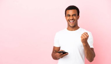 Telif uzayındaki Afrikalı Amerikalı adam. Pembe arka plan. Telefon zafer pozisyonunda.